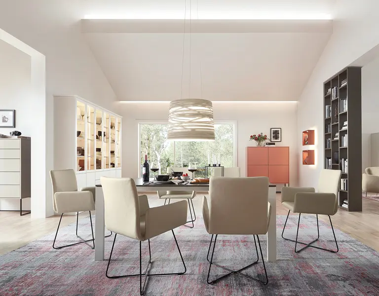 Helles Esszimmer mit modernen cremefarbenen Polsterstühlen, großer Glasvitrine und dekorativem Esstisch, ergänzt durch stilvolle Pendelleuchte und offenes Regal für eine elegante Raumgestaltung.